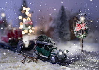 Fototapeta premium Miniature classic car carrying a christmas tree and gifts on snowy road in winter background