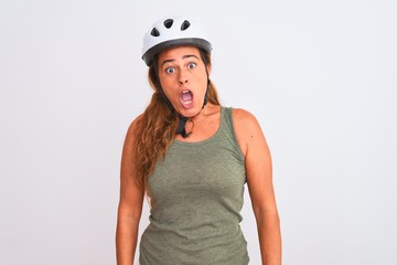 Middle age mature cyclist woman wearing safety helmet over isolated background In shock face, looking skeptical and sarcastic, surprised with open mouth