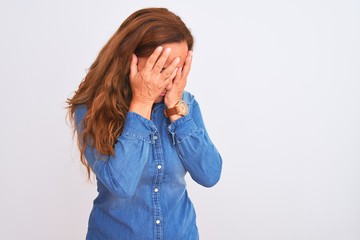 Middle age mature woman wearing denim jacket standing over white isolated background with sad expression covering face with hands while crying. Depression concept.