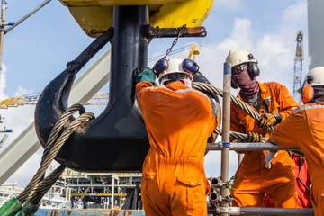 Offshore workers installing a heavy lifting sling onto a crane hook on board a construction work barge at oil field - Powered by Adobe