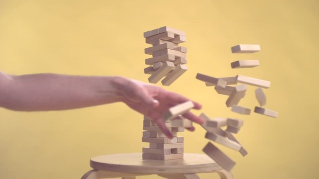 Hands Of Young Man Plays Jenga On Yellow Background slow motion