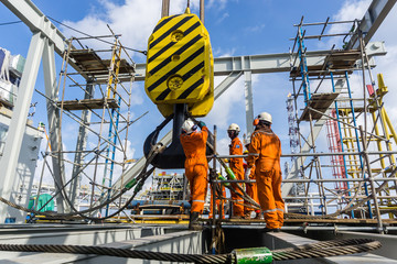 Offshore workers performing inspection to a crane hook and rigging arrangement prior to heavy lift - obrazy, fototapety, plakaty