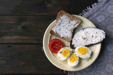food of the poor, minimalism. Bread toasts are spread with soft cheese, boiled eggs and tomatoes on a yellow plate.