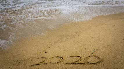 Numbers 2020 year on the sea shore, message handwritten in the golden sand on beautiful beach background.