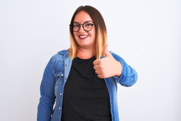 Young beautiful woman wearing denim shirt and glasses over isolated white background doing happy thumbs up gesture with hand. Approving expression looking at the camera with showing success.