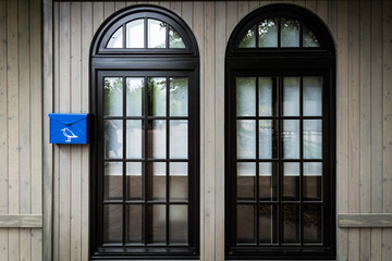 Two large black window in art Nouveau style and a small blue mailbox next to them