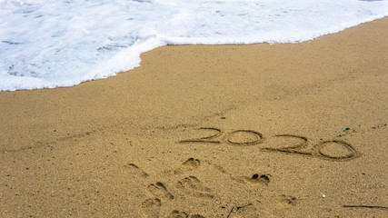 Numbers 2020 year on the sea shore, message handwritten in the golden sand on beautiful beach background.