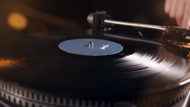 One person places a black disk onto a vinyl player and pushes a button.