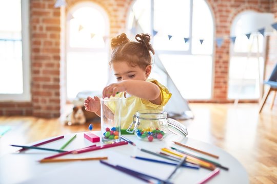 Beautiful toddler standing playing with chocolate colored balls on the table at kindergarten