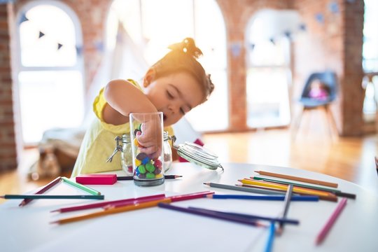 Beautiful toddler standing playing with chocolate colored balls on the table at kindergarten