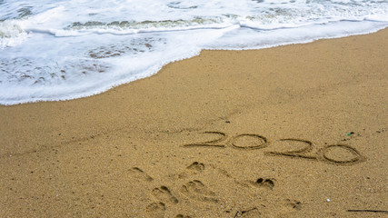 Numbers 2020 year on the sea shore, message handwritten in the golden sand on beautiful beach background.
