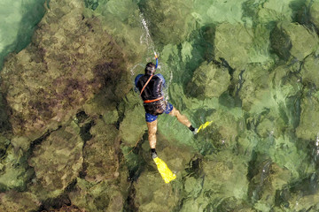 Aerial view of a Man Snorkelling for treasure in crystal clear water at sea.