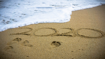Numbers 2020 year on the sea shore, message handwritten in the golden sand on beautiful beach background.