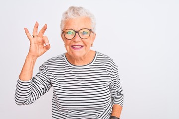 Senior grey-haired woman wearing striped navy t-shirt glasses over isolated white background smiling positive doing ok sign with hand and fingers. Successful expression.