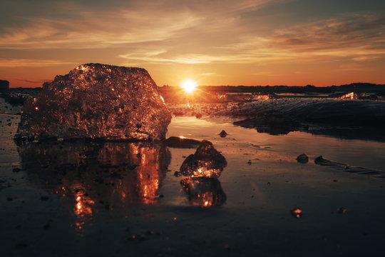 Pieces of beautiful transparent ice in pink and amber colors as a jewels shining on a frozen seashore in the sunset