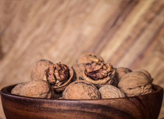 walnuts in a wooden bowl closeup. background with whole walnuts and halves of nuts.