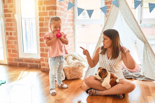 Beautiful teacher sitting on the floor getting angry with blond toddler girl outside tipi at kindergarten