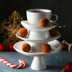White saucer pyramid with cup of tea on top, like Christmas tree with decorated with sweet chocolate truffles, dark background Creative concept, restaurant, wallpaper, postcard, Xmas, New Year, Square