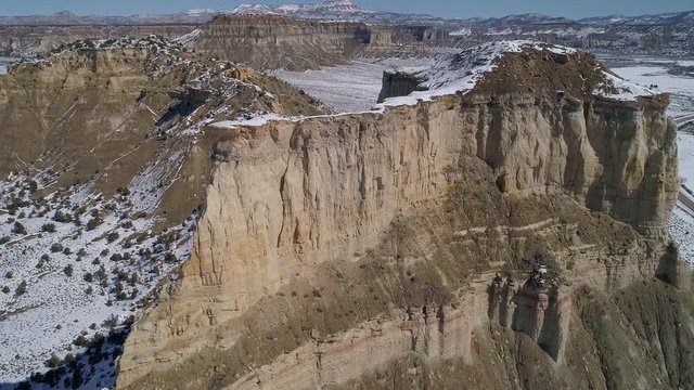 Rotating aerial view of mesa half covered in snow along HWY 12 in the Utah desert in winter.