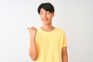 Chinese man wearing yellow casual t-shirt standing over isolated white background smiling with happy face looking and pointing to the side with thumb up.