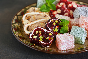 National Turkish dessert. Plate with various pieces of turkish delight lokum on a dark concrete background.