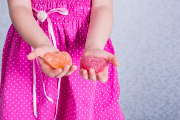 little girl stretching two marmalade hearts in her palms. Valentine's Day, Love Day. Children Protection Day