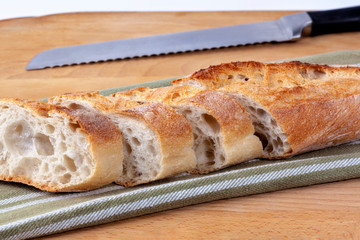 Slices of freshly baked French baguette with bread knife on an olive striped cotton fabric as a catering concept. Feature crispy crusts and airy centers.
