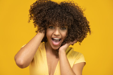 Happy laughing American African woman with her curly hair on yellow background. Laughing curly woman in sweater touching her hair and looking at the camera.