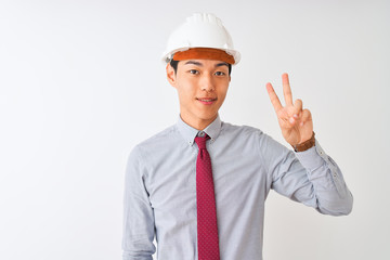 Chinese architect man wearing tie and helmet standing over isolated white background showing and pointing up with fingers number two while smiling confident and happy.