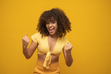 Young beautiful brunette curly hair girl happily rejoicing saying yes on yellow background. Success and achievement concept. Cheerful pretty woman on yellow background.