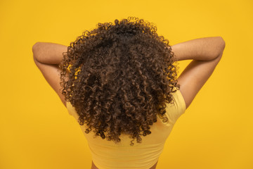 Backwards American African woman with her curly hair on yellow background. Laughing curly woman in...