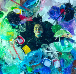 Woman drowning in water under plastic recipients pile, garbage. Used bottles and packs filling world ocean killing people. Ecology, environment concept, plastic and glass pollution, nature disaster.
