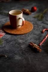 Christmas background, on the stand a red Cup of tea. Christmas decorations, holiday decorations, fir branches, red balls, cinnamon and red Lollipop cane on dark stone background top view.