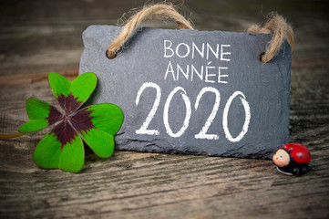 Chalkboard with four leaf clover and chimney sweeper and sparklers with bonne annee 2020 on wooden...