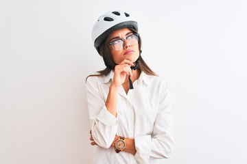 Beautiful businesswoman wearing glasses and bike helmet over isolated white background with hand on chin thinking about question, pensive expression. Smiling with thoughtful face. Doubt concept.