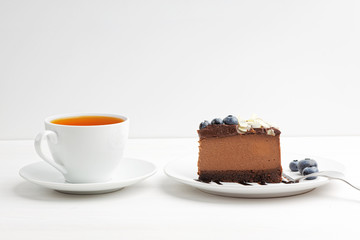 Closeup cup of tea and piece of homemade chocolate cheesecake with blueberries and almond slices on white wooden table. Front view. Copy space.