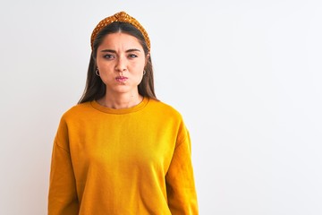 Young beautiful woman wearing yellow sweater and diadem over isolated white background puffing cheeks with funny face. Mouth inflated with air, crazy expression.