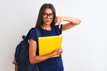 Young student woman wearing backpack glasses holding book over isolated white background with angry face, negative sign showing dislike with thumbs down, rejection concept