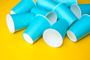 Many blue paper disposable cups on yellow background. Set for party. Top view. Minimalist Style. Copy, empty space for text