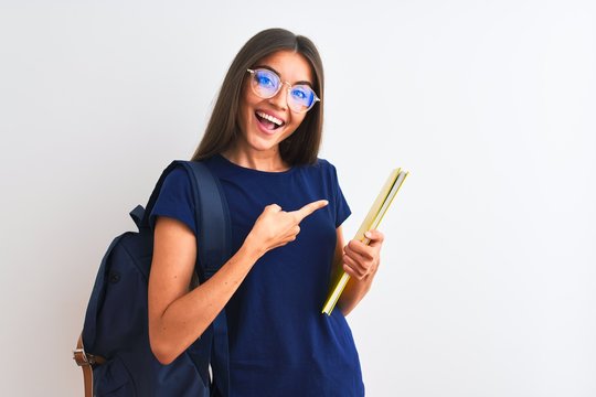 Young student woman wearing backpack glasses holding book over isolated white background very happy pointing with hand and finger