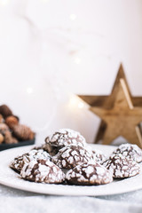 Home baked chocolate crinkle cookies in icing sugar.  Cracked chocolate biscuits in a white plate on Christmas background. Chocolate Christmas brown cookies in powdered sugar with cracks. Copy space.