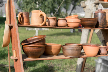 Fototapeta premium Ceramics fair in Park. Clay dishes on wooden shelf. Pottery craft. Kitchen utensils. Folk art. Everyday life. Household goods