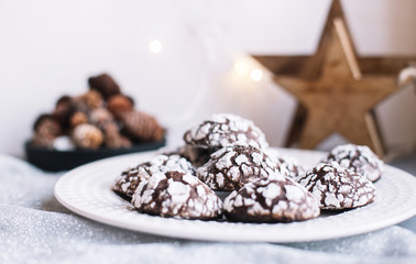 Home baked chocolate crinkle cookies in icing sugar.  Cracked chocolate biscuits in a white plate on Christmas background. Chocolate Christmas brown cookies in powdered sugar with cracks. Copy space.