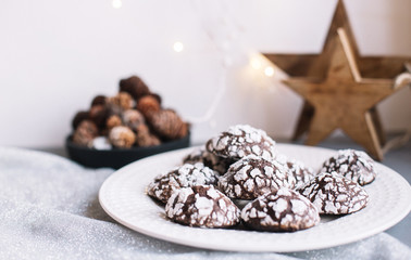 Home baked chocolate crinkle cookies in icing sugar.  Cracked chocolate biscuits in a white plate on Christmas background. Chocolate Christmas brown cookies in powdered sugar with cracks. Copy space.
