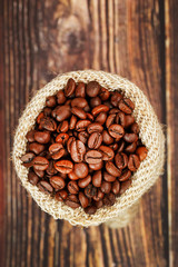 Freshly roasted aromatic coffee in a burlap bag on a wooden background.