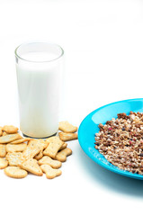Muesli flakes in blue plate, cookies and glass of milk on white background