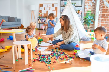 Beautiful teacher and group of toddlers playing around lots of toys at kindergarten