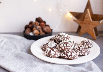 Home baked chocolate crinkle cookies in icing sugar.  Cracked chocolate biscuits in a white plate on Christmas background. Chocolate Christmas brown cookies in powdered sugar with cracks. Copy space.