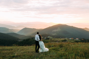 Fototapeta na wymiar Newlyweds enjoy sunset in the mountains, view from the back