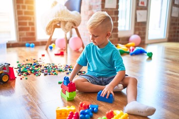 Young caucasian kid playing at kindergarten with toys. Preschooler boy happy at playroom.